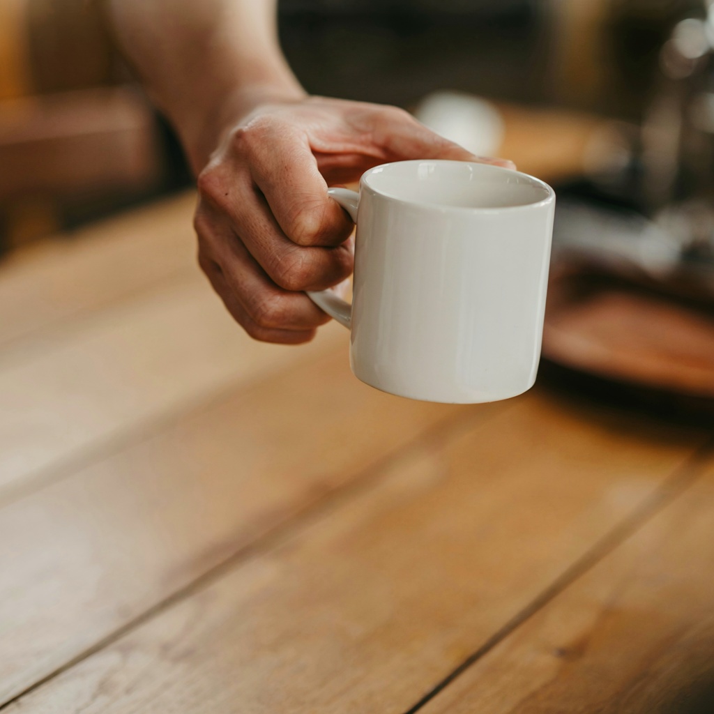 A person holding a white ceramic coffee mug by the handle wi
