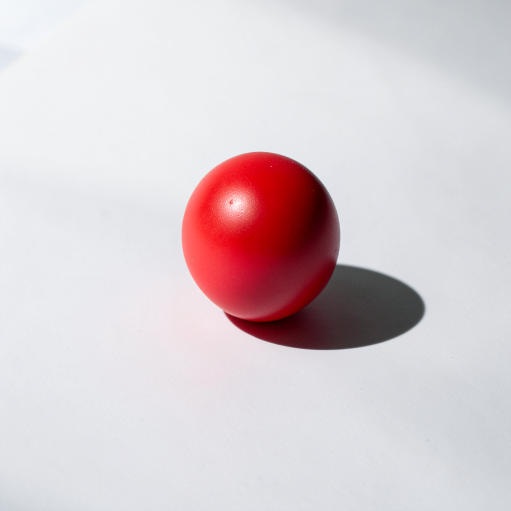 A red sphere on a white surface with a single shadow cast to