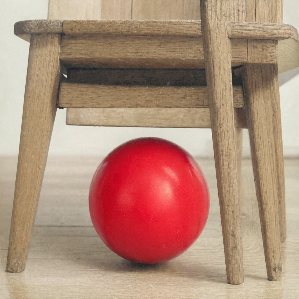 A red ball underneath a wooden chair