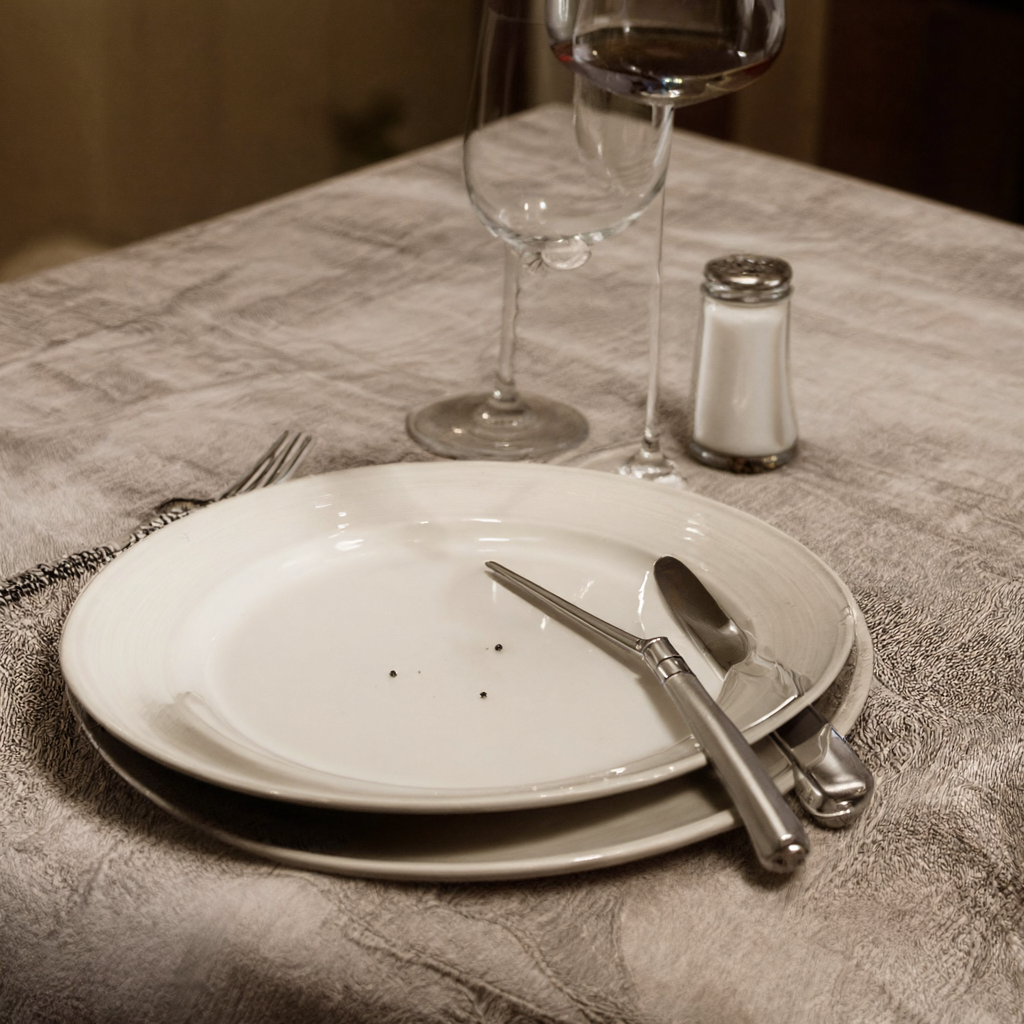 A dinner table scene with a plate, fork, knife, wine glass, 