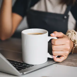 A person holding a white ceramic coffee mug by the handle wi