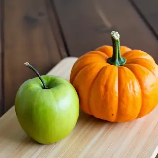 A green apple and an orange pumpkin on a wooden cutting boar