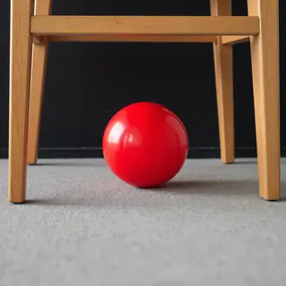 A red ball underneath a wooden chair