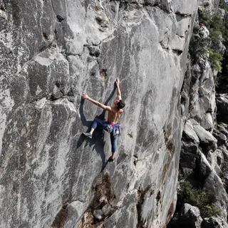 A rock climber clinging to a cliff face with arms and legs e