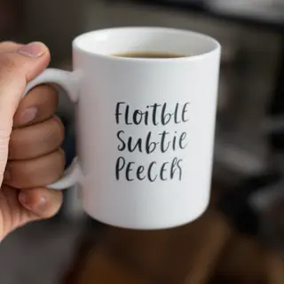 A person holding a white ceramic coffee mug by the handle wi