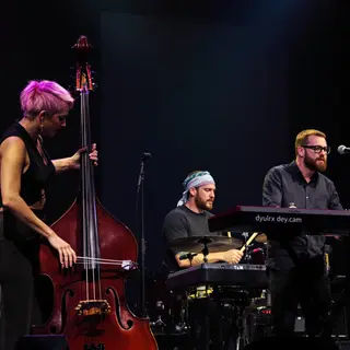 Three musicians on stage: a tall woman with short pink hair 