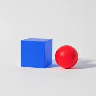 A red ball and a blue cube sitting side by side on a white s