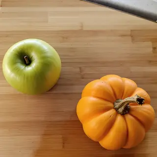 A green apple and an orange pumpkin on a wooden cutting boar