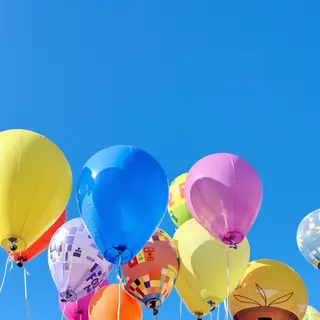 Exactly 11 colorful balloons floating against a clear blue s