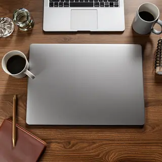 A workspace desk with a brushed aluminum laptop, a leather-b