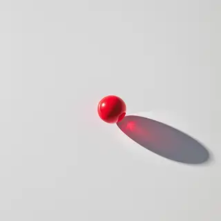A red sphere on a white surface with a single shadow cast to