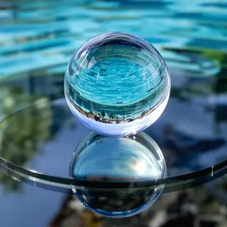 A clear glass sphere sitting on a mirror surface near a pool