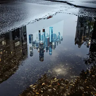 A city skyline reflected in a rain puddle on a street, with 