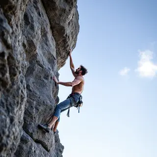 A rock climber clinging to a cliff face with arms and legs e