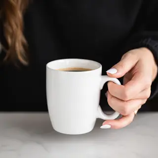 A person holding a white ceramic coffee mug by the handle wi