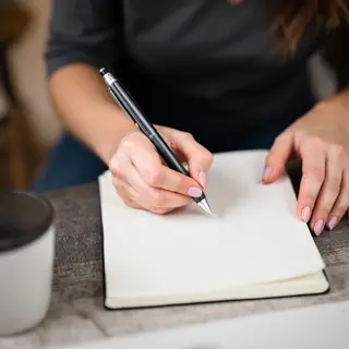 A woman writing in a notebook with a pen gripped correctly i