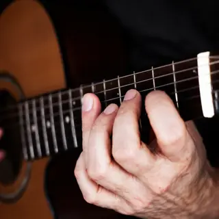 A person playing an acoustic guitar with left hand on the fr