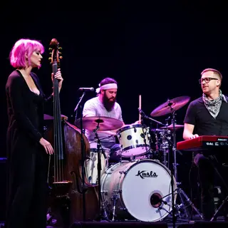 Three musicians on stage: a tall woman with short pink hair 