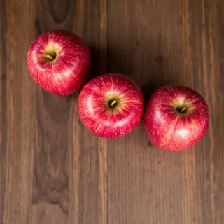 Exactly 3 red apples arranged on a wooden table