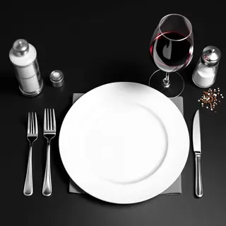 A dinner table scene with a plate, fork, knife, wine glass, 