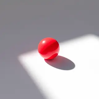 A red sphere on a white surface with a single shadow cast to