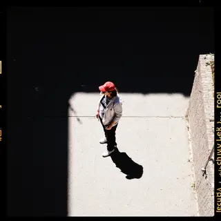 A person standing outdoors at midday with a short shadow dir