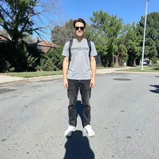 A person standing outdoors at midday with a short shadow dir
