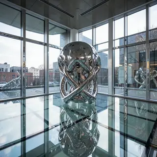 A chrome sculpture in a room with a glass floor and large wi
