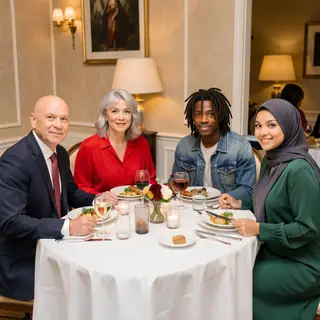 Four people at a dinner table: a bald man in a suit, a woman