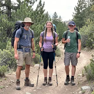 Three hikers on a trail: a man with a backpack and sunhat, a