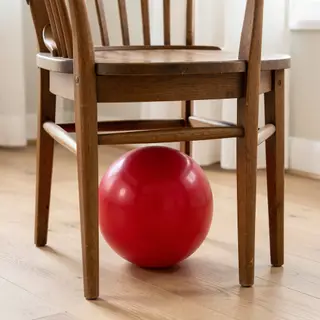 A red ball underneath a wooden chair