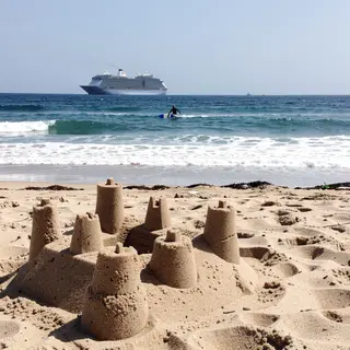 A beach scene with a sandcastle in the foreground, a surfer 