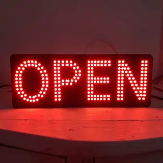 The word 'OPEN' displayed on a red LED sign with glowing pix