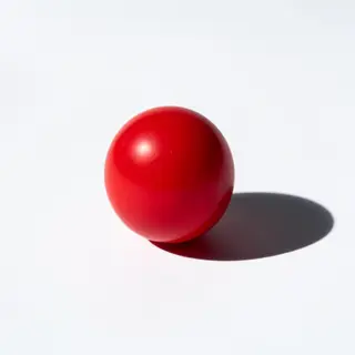 A red sphere on a white surface with a single shadow cast to