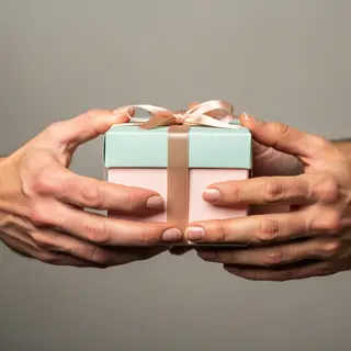One person handing a small gift box to another person, both 