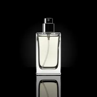 A clear glass perfume bottle on a reflective black surface w