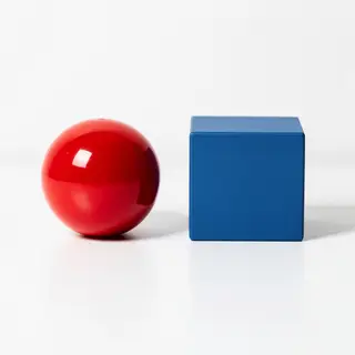 A red ball and a blue cube sitting side by side on a white s