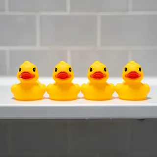 Exactly 5 yellow rubber ducks sitting in a row on a bathroom
