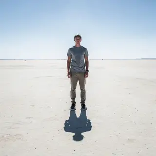 A person standing outdoors at midday with a short shadow dir