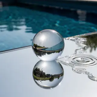A clear glass sphere sitting on a mirror surface near a pool
