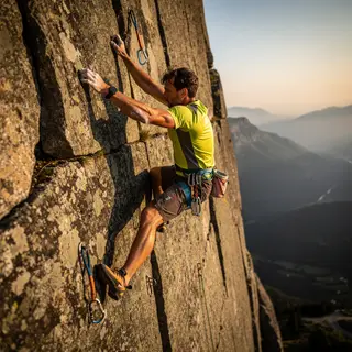 A rock climber clinging to a cliff face with arms and legs e