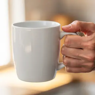 A person holding a white ceramic coffee mug by the handle wi