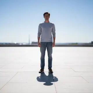 A person standing outdoors at midday with a short shadow dir
