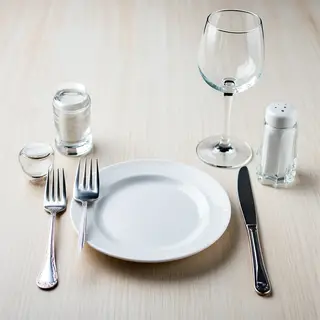 A dinner table scene with a plate, fork, knife, wine glass, 