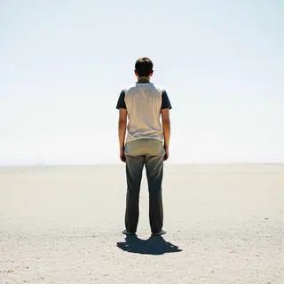 A person standing outdoors at midday with a short shadow dir