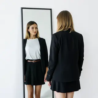 A woman standing in front of a full-length mirror, her refle