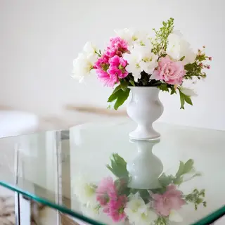 A vase of flowers on a glass table with a clear reflection v