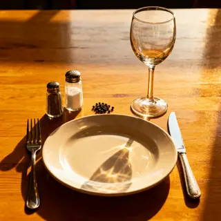 A dinner table scene with a plate, fork, knife, wine glass, 