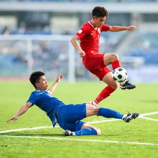 Two soccer players mid-tackle, one sliding and the other jum
