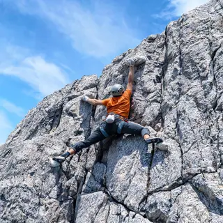A rock climber clinging to a cliff face with arms and legs e